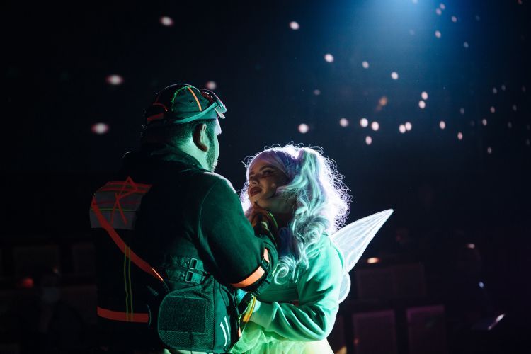 Two singers perform on stage in futuristic costumes under mirror ball lighting